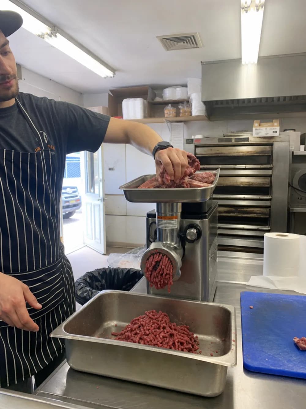 A cook feeding beef into the countertop grinder on the prep table